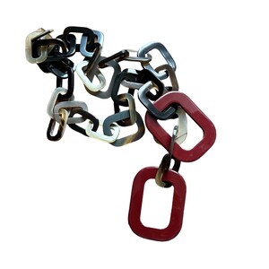 May include: A red, black, and brown chain necklace with a large red rectangular pendant. The chain is made of plastic and has a link design. The pendant is also made of plastic and has a smooth surface.