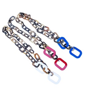 May include: Three layered chains made of brown and beige plastic links with a square shape. Each chain has a different colored square link at the end: white, red, and blue.