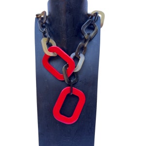 May include: A red and brown plastic necklace with large, rectangular links. The necklace is displayed on a black mannequin.