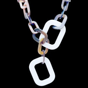 May include: A white and brown plastic necklace with a chain link design. The necklace has two large white square links and a smaller white square link at the bottom.