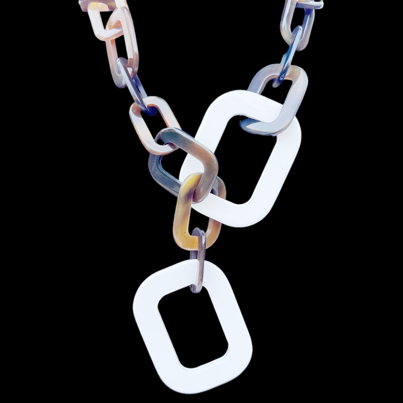 May include: A white and brown plastic necklace with a chain link design. The necklace has two large white square links and a smaller white square link at the bottom.