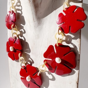 May include: A red flower necklace with white pearl accents. The necklace is made of plastic and has a chain link design.