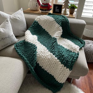 May include: A green and white striped chunky knit throw blanket draped over a sofa with a white throw pillow that says "Home Happy Place".