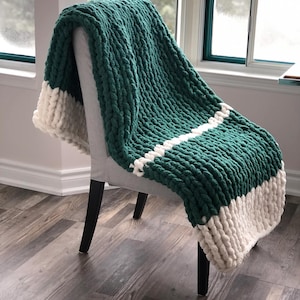 May include: A chunky knit throw blanket in a deep green color with white stripes. The blanket is draped over a chair.