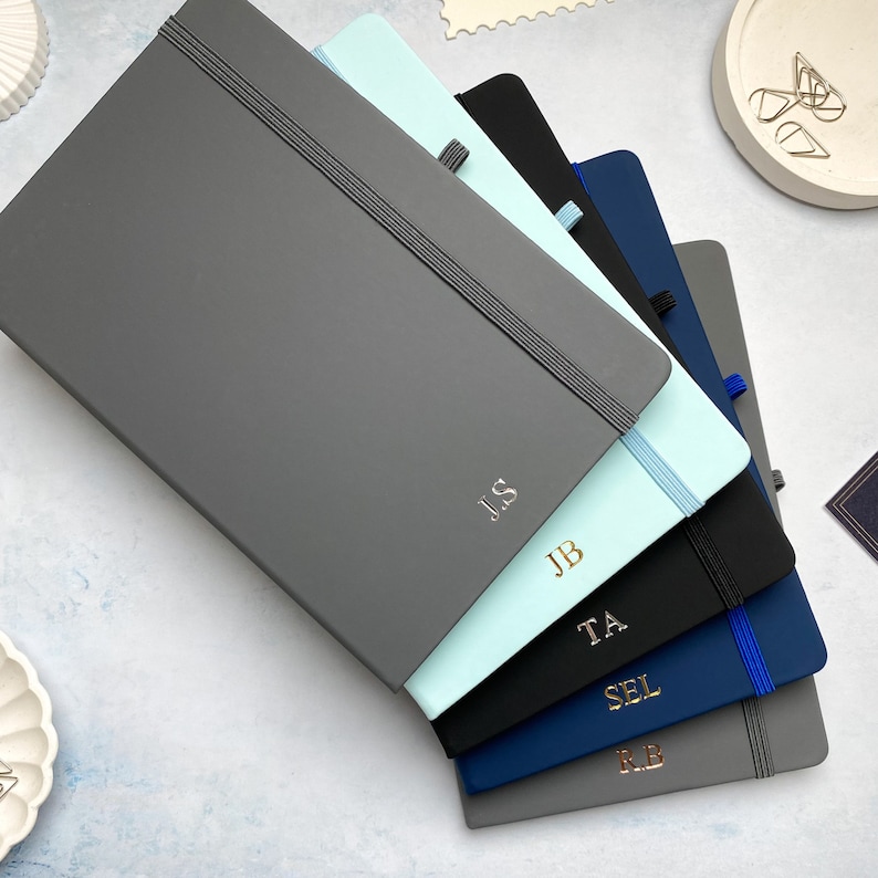 A5 notebooks with personalised initials foil printed centrally at the bottom of the covers. Blue, grey and black notebooks.