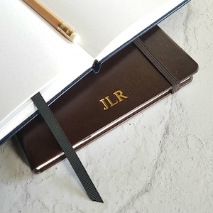May include: A brown leather-bound journal with a black ribbon bookmark and gold embossed initials "JLR".