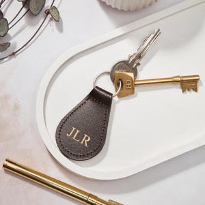 May include: A brown leather keyring with the initials "JLR" embossed in gold. The keyring is attached to a set of keys with a gold-coloured key.