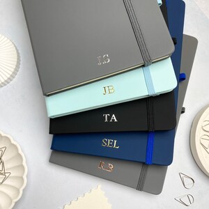 A5 notebooks with personalised initials on the covers. Blue, grey and black notebooks.