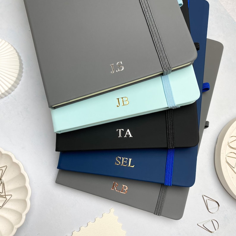 A5 notebooks with personalised initials on the covers. Blue, grey and black notebooks.