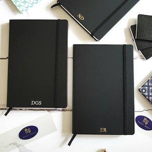 Black A5 notebooks with gold or silver personalised initials on the bottom of the journal cover.