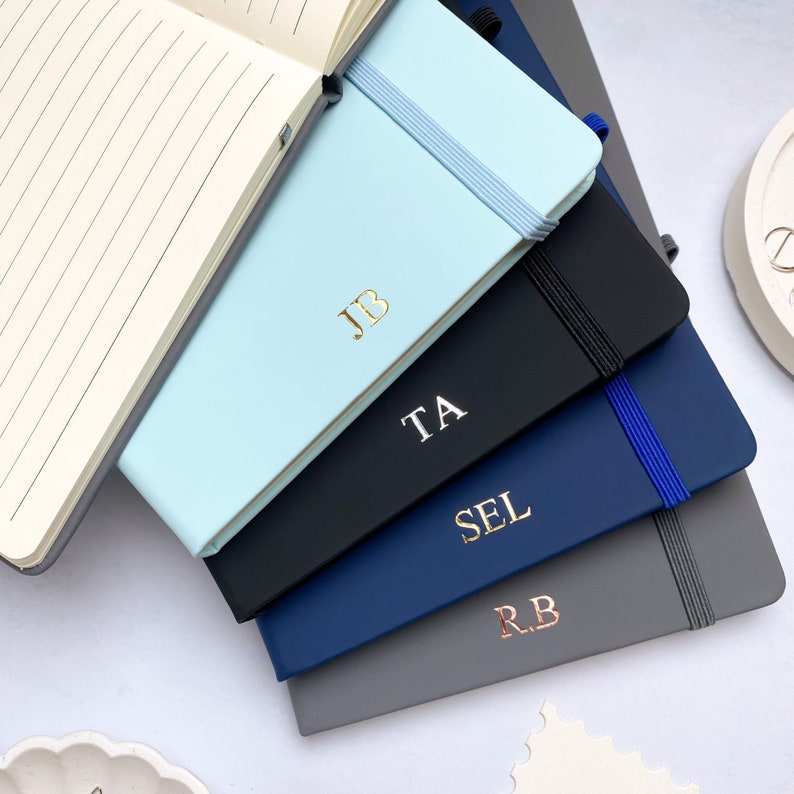 A5 notebooks with personalised initials on the covers and lined paper. Blue, grey and black journals.