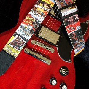 以下が含まれることがあります： 黒いピックガードが付いた赤いエレキギターと、ビンテージホラー映画のポスターがついたギターストラップ。ストラップには、「アタック・オブ・ザ・パペット・ピープル」、「ジャイアント・スパイダー・ストライクス」、「タランチュラ」、「モンスター・オン・ザ・キャンパス」、「シュリンキング・マン」、「ザ・ブレイン・ザット・ウッドント・ダイ」、「アタック・オブ・ザ・パペット・ピープル」のタイトルが書かれている。