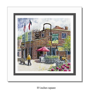 May include: Watercolor painting of a brick building with the text "Downtown Boone" and "Appalachian". The artwork includes a red umbrella, flowers, and people. The painting is 10 inches square.