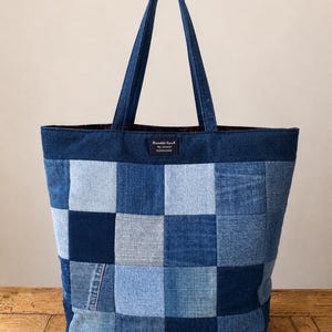 May include: A tote bag constructed from a patchwork of various blue denim fabric squares. The bag features two long shoulder straps and a small rectangular black label near the top centre with the text Rinaldi SpA TEL 242431 FUCECCHIO.