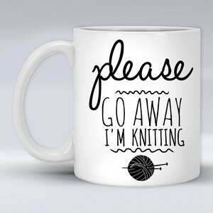 May include: White ceramic mug with a black design that says "please go away i'm knitting" with a black and white illustration of a ball of yarn and knitting needles.