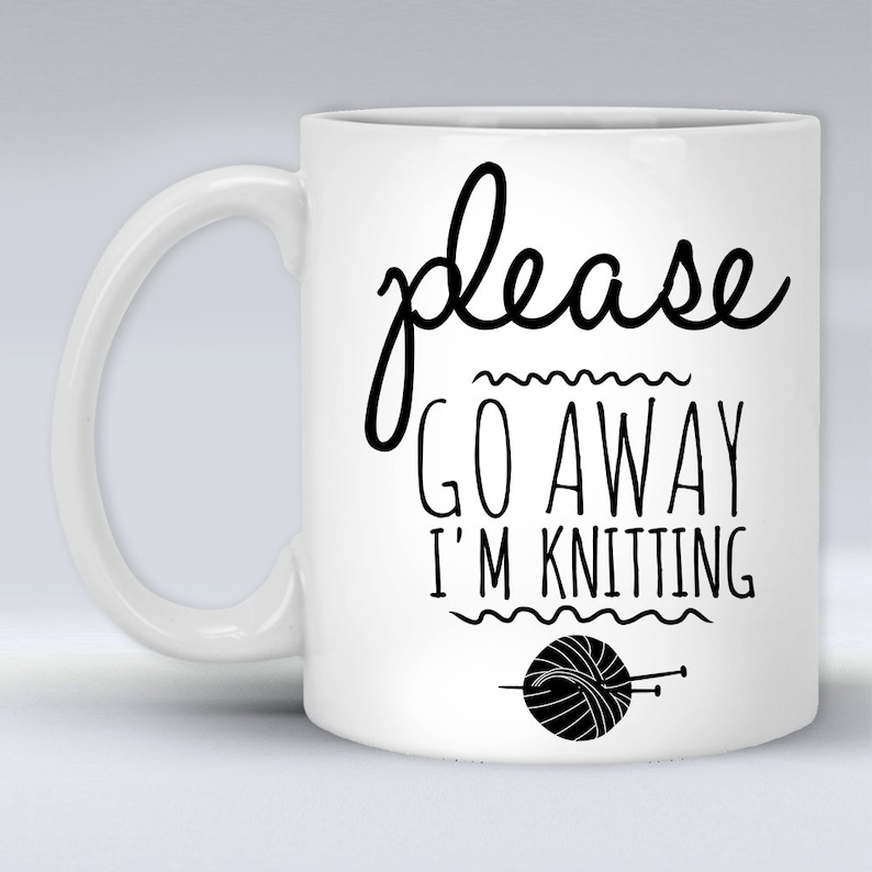 May include: White ceramic mug with a black design that says "please go away i'm knitting" with a black and white illustration of a ball of yarn and knitting needles.