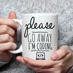 Puede incluir: Taza de cerámica blanca con texto negro que dice "please go away i'm coding" y un icono en blanco y negro de un portátil con corchetes angulares.