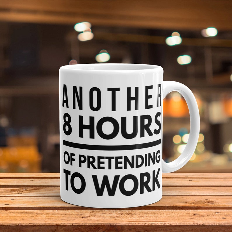 May include: White ceramic coffee mug with black text that reads "Another 8 Hours of Pretending to Work".
