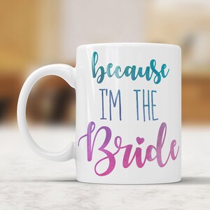 May include: White ceramic coffee mug with a blue and pink ombre design. The mug says "because I'm the Bride" with a small heart.