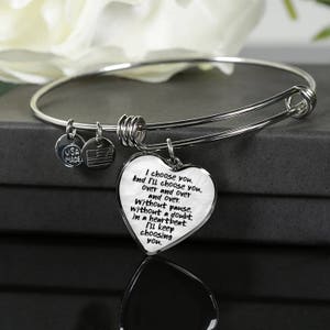 May include: A silver bangle bracelet with a heart-shaped charm that reads "I choose you. And I'll choose you. over and over and over. Without pause. without a doubt. in a heartbeat. I'll keep choosing you."