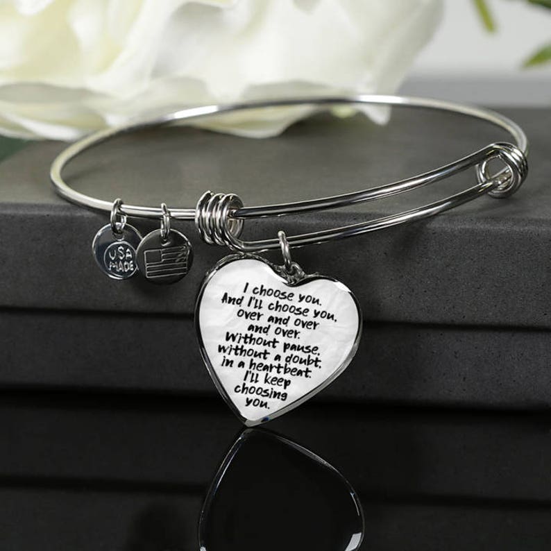 May include: A silver bangle bracelet with a heart-shaped charm that reads "I choose you. And I'll choose you. over and over and over. Without pause. without a doubt. in a heartbeat. I'll keep choosing you."