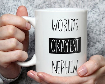 May include: White ceramic mug with black text that reads "World's Okayest Nephew".