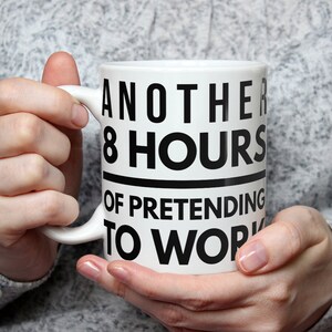 May include: White ceramic mug with black text that reads "Another 8 hours of pretending to work".
