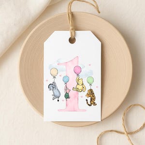 A white tag with a pink number one and illustrations of Winnie the Pooh and Tigger holding balloons.