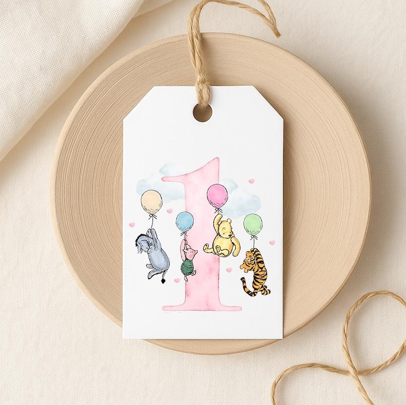 A white tag with a pink number one and illustrations of Winnie the Pooh and Tigger holding balloons.