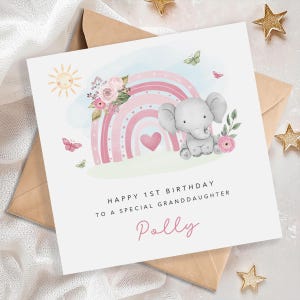 May include: A square greeting card featuring a watercolor illustration of a gray elephant, a pink rainbow, a heart, flowers, butterflies, and a sun. The text reads: HAPPY 1ST BIRTHDAY TO A SPECIAL GRANDDAUGHTER, followed by the name Polly in pink.