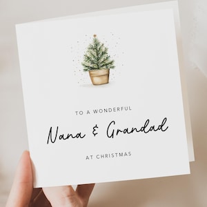 May include: A square white greeting card featuring a watercolor illustration of a small green Christmas tree in a tan pot. The text reads: TO A WONDERFUL Nana & Grandad AT CHRISTMAS. The design includes small gold speckles around the tree.