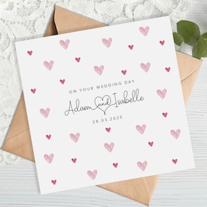 May include: A white wedding card with pink watercolour hearts and the text "On your wedding day Adam and Isabelle 28.03.2025"