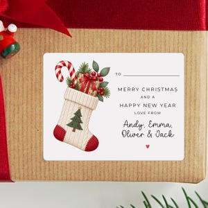 May include: A rectangular white gift tag sticker featuring a cream-coloured knit Christmas stocking filled with a candy cane, a gift box, and greenery. The text reads: TO, MERRY CHRISTMAS AND A HAPPY NEW YEAR, LOVE FROM, Andy, Emma, Oliver & Jack.