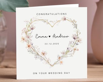 May include: A square wedding card with a floral heart design. The card reads "Congratulations" at the top, with the names "Emma" and "Andrew" and the date "22.12.2025" in the center. The bottom of the card says "On Your Wedding Day."