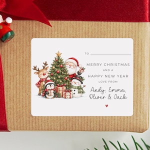 May include: A rectangular white gift tag sticker featuring a festive illustration of Santa Claus, a reindeer, a penguin, and a snowman around a decorated Christmas tree with gifts. The text reads: TO, MERRY CHRISTMAS AND A HAPPY NEW YEAR, LOVE FROM Andy, Emma, Oliver & Jack.