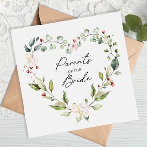 May include: A white card with a green and pink floral heart design. The text "Parents of the Bride" is written in black cursive lettering.