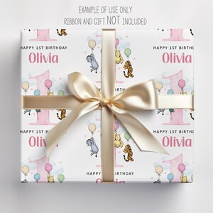 The image is a gift box with a white background and a gold ribbon. The gift box has a repeating pattern of Winnie the Pooh characters and balloons, and the name "Olivia" is written on it.