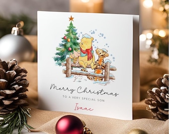 May include: A white square greeting card featuring a watercolor illustration of Winnie the Pooh, Piglet, and Tigger sitting on a wooden fence near a decorated Christmas tree. The text reads Merry Christmas TO A VERY SPECIAL SON Isaac.