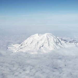 May include: A snow-capped mountain peak rises above a sea of white clouds, with a clear blue sky above.