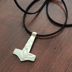 Puede incluir: Collar con colgante de Mjolnir de plata con acabado martillado, colgado de un cordón de cuero negro.