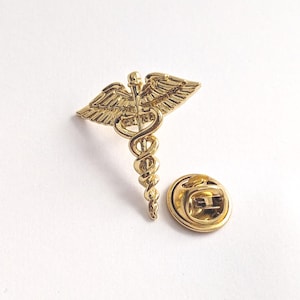 Caduceus pin. Classic medical symbol plated in gold. Elegance and meaning in a distinctive piece of jewelry.