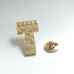 Può includere: Spilla dorata con un designo dettagliato che presenta un sole, una luna e altri simboli. La spilla ha un design a forma di T e una chiusura di sicurezza sul retro.