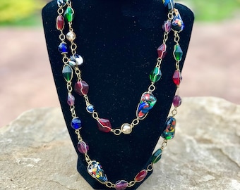 May include: A multi-strand necklace with gold chain links and colorful glass beads. The beads are various shapes and sizes, including round, oval, and teardrop. The necklace is displayed on a black velvet bust.