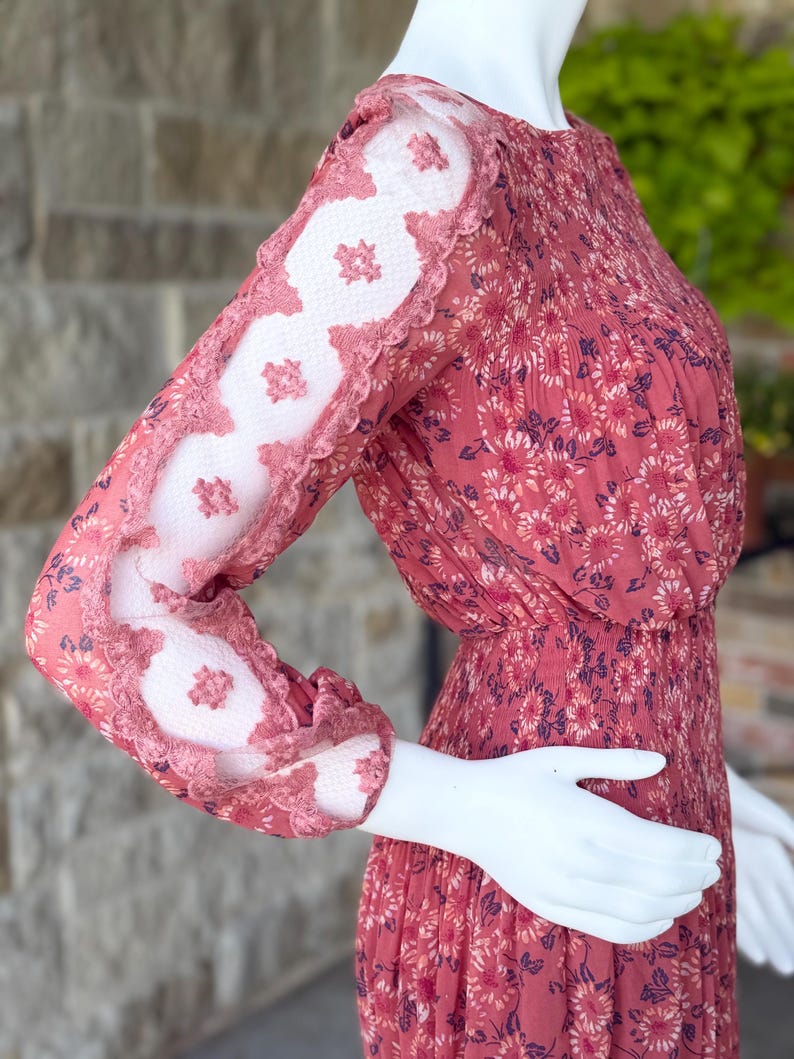Pode incluir: Vestido de manga comprida com estampa floral em tons de vermelho e rosa. As mangas apresentam um design de renda exclusivo com uma borda ondulada. O vestido &eacute; exibido em um manequim.