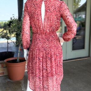Pode incluir: Vestido coral com estampa floral, mangas compridas e costas com abertura. O vestido apresenta um corpete franzido e uma saia fluida. O vestido &eacute; exibido em um manequim.