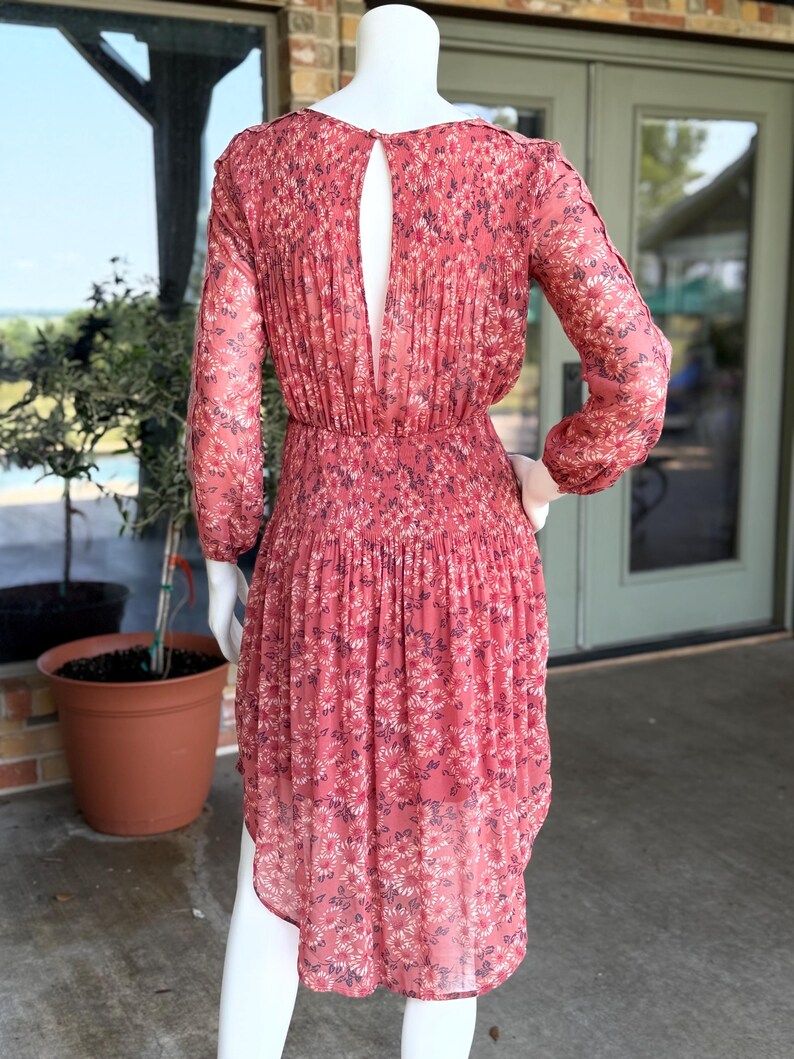Pode incluir: Vestido coral com estampa floral, mangas compridas e costas com abertura. O vestido apresenta um corpete franzido e uma saia fluida. O vestido &eacute; exibido em um manequim.