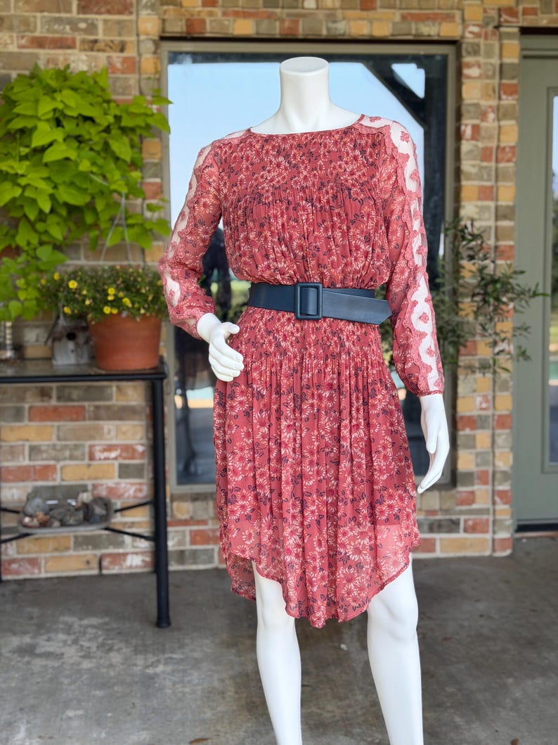 Pode incluir: Vestido vermelho com estampa floral, mangas compridas e cinto preto. O vestido tem uma saia fluida e &eacute; exibido em um manequim. As mangas t&ecirc;m um design transparente semelhante a renda. O vestido &eacute; na altura do joelho.
