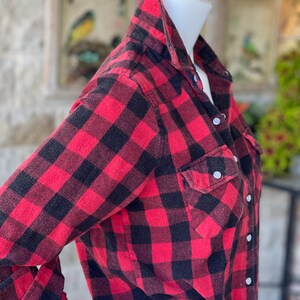 May include: A red and black plaid flannel shirt with long sleeves and a button-up front.