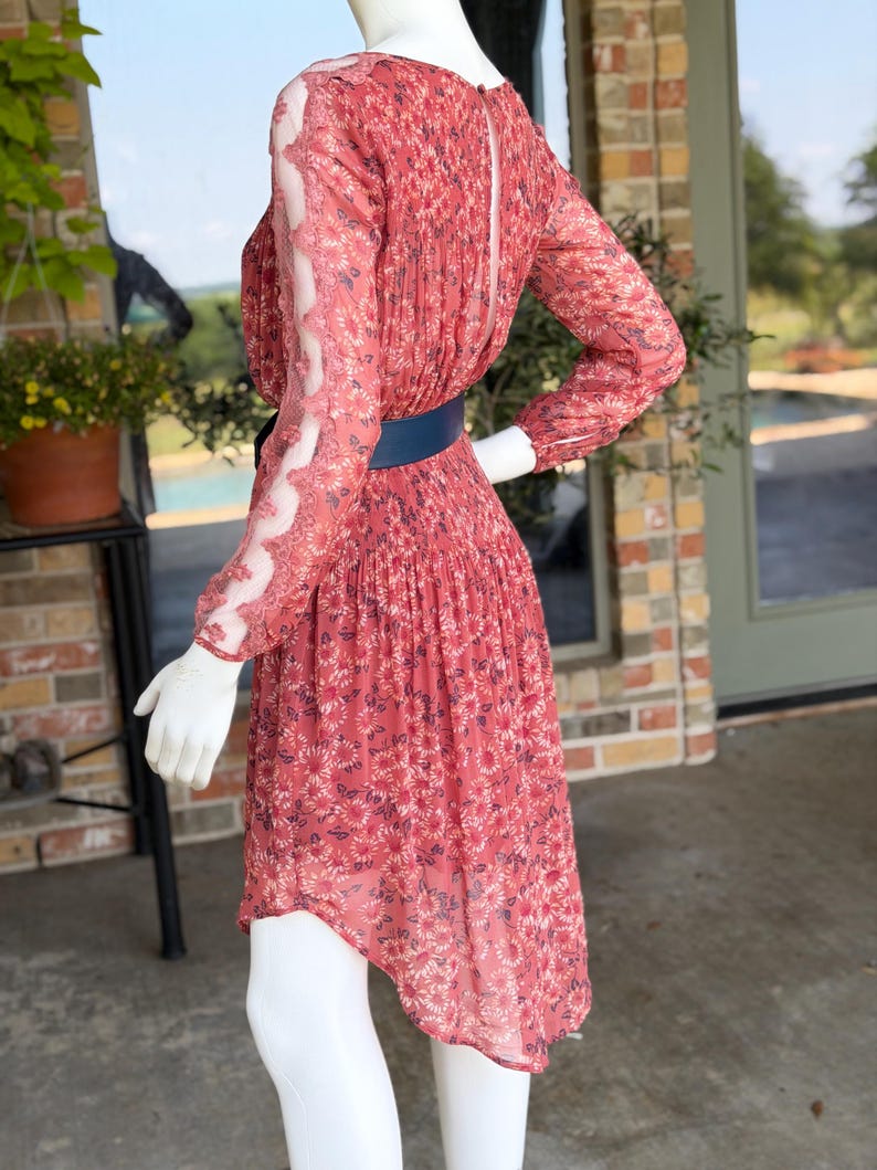 Pode incluir: Um vestido vermelho com estampa floral, mangas compridas e cinto azul. O vestido tem uma saia plissada e mangas transparentes com detalhes em renda. O vestido &eacute; exibido em um manequim.