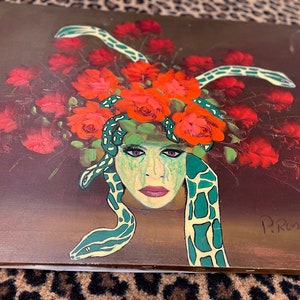 May include: A painting of a woman's face with snakes and red roses around her head. The woman has green eyes and is wearing a green and white snake-skin patterned headpiece. The painting is signed "P. Rossi" in the bottom right corner.